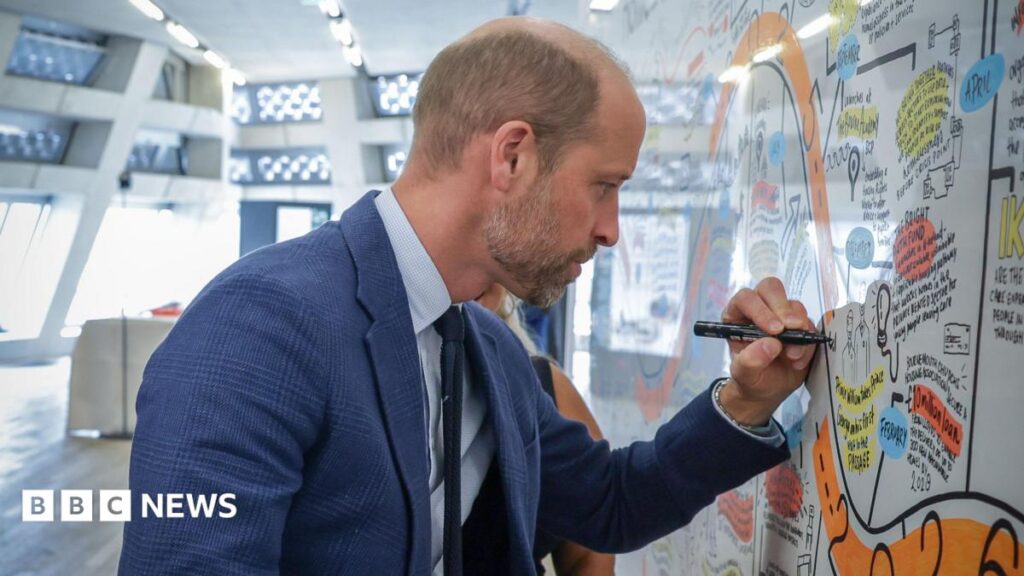 Prince William, wearing a blue checked blazer, signing artwork with a black marker.