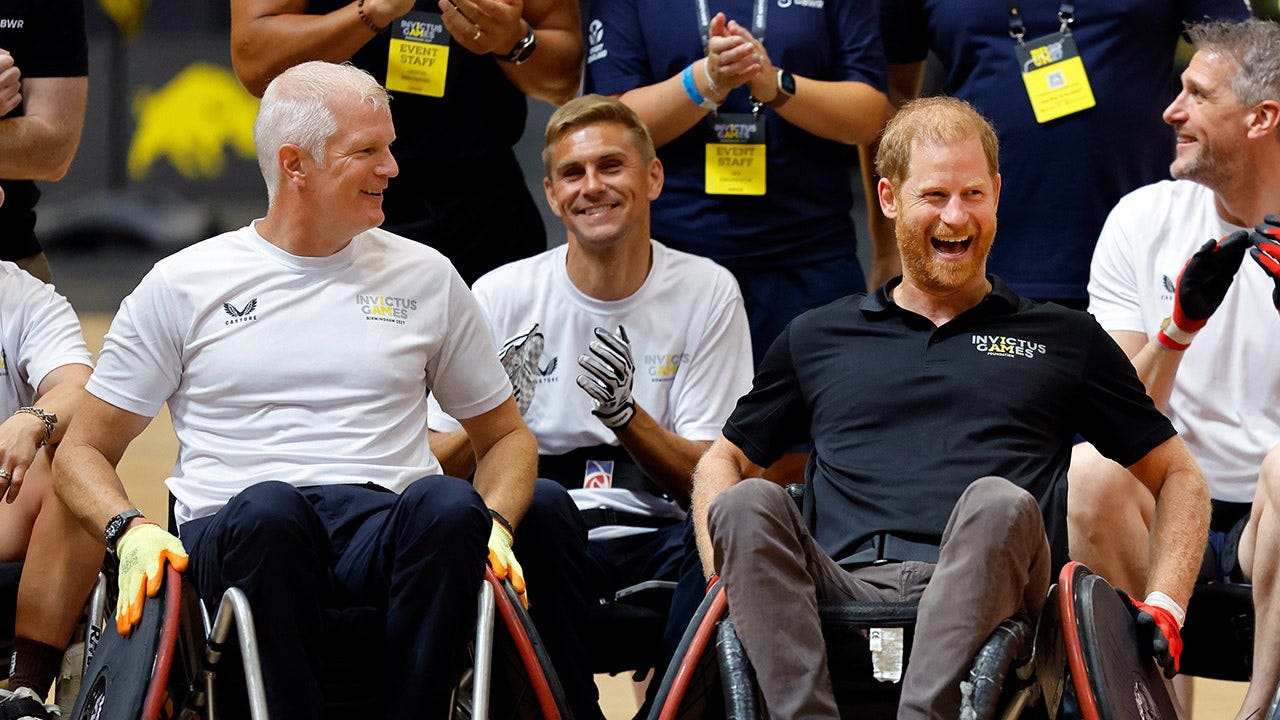 Al Carns and Prince Harry play wheelchair rugby in a gymnasium.