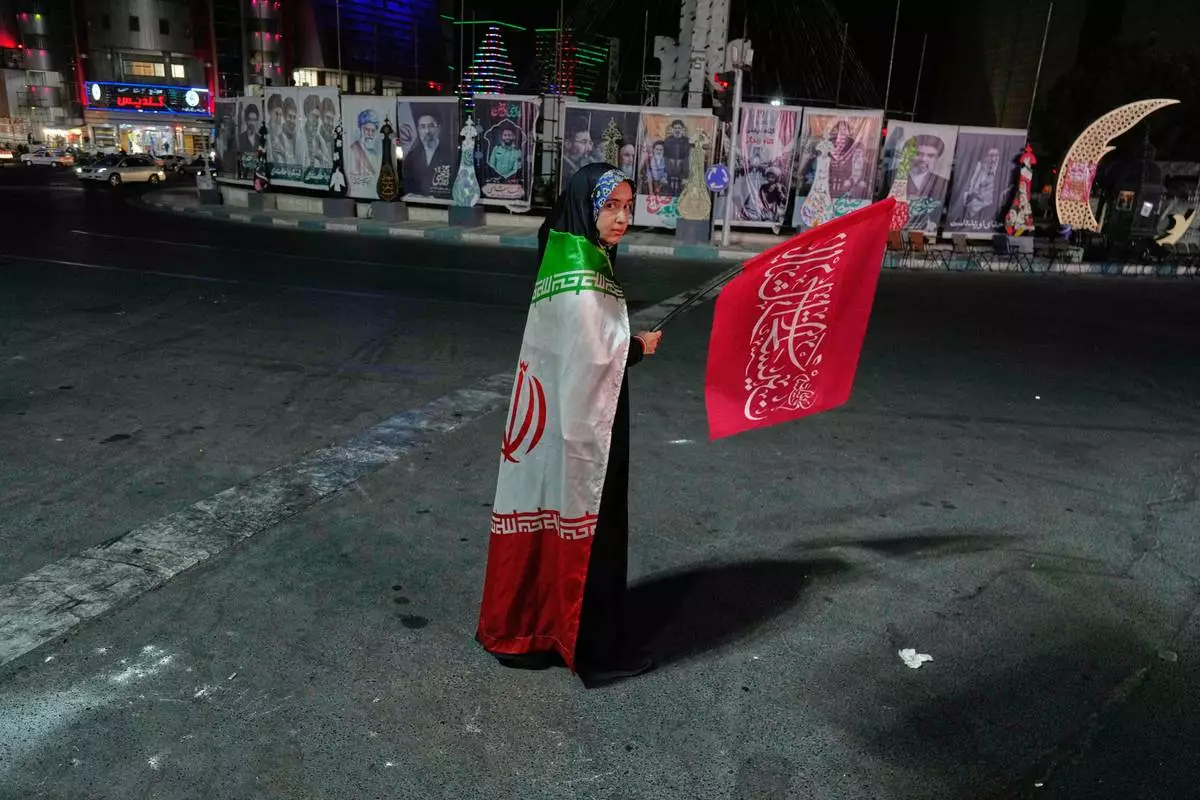 A pro-government demonstrator wears an Iranian flag as she waves a religious flag in a gathering commemorating the late Iranian Supreme Leader Ayatollah Ali Khamenei at a square in Tehran, Saturday, July 11, 2026. (AP Photo/Vahid Salemi)