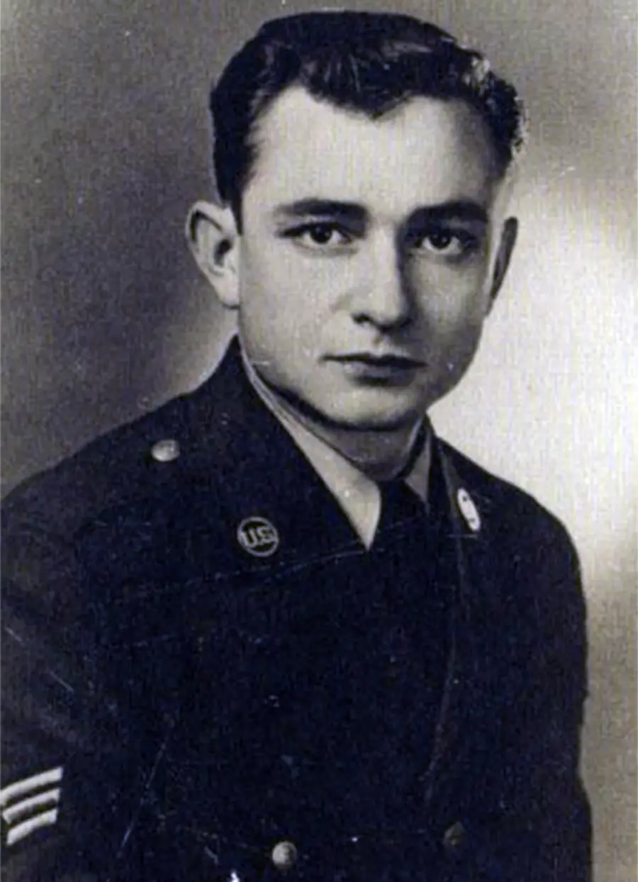 Black and white portrait of a young man in a U.S. military uniform, looking at the camera with a neutral expression. The background is plain and the photo appears vintage.