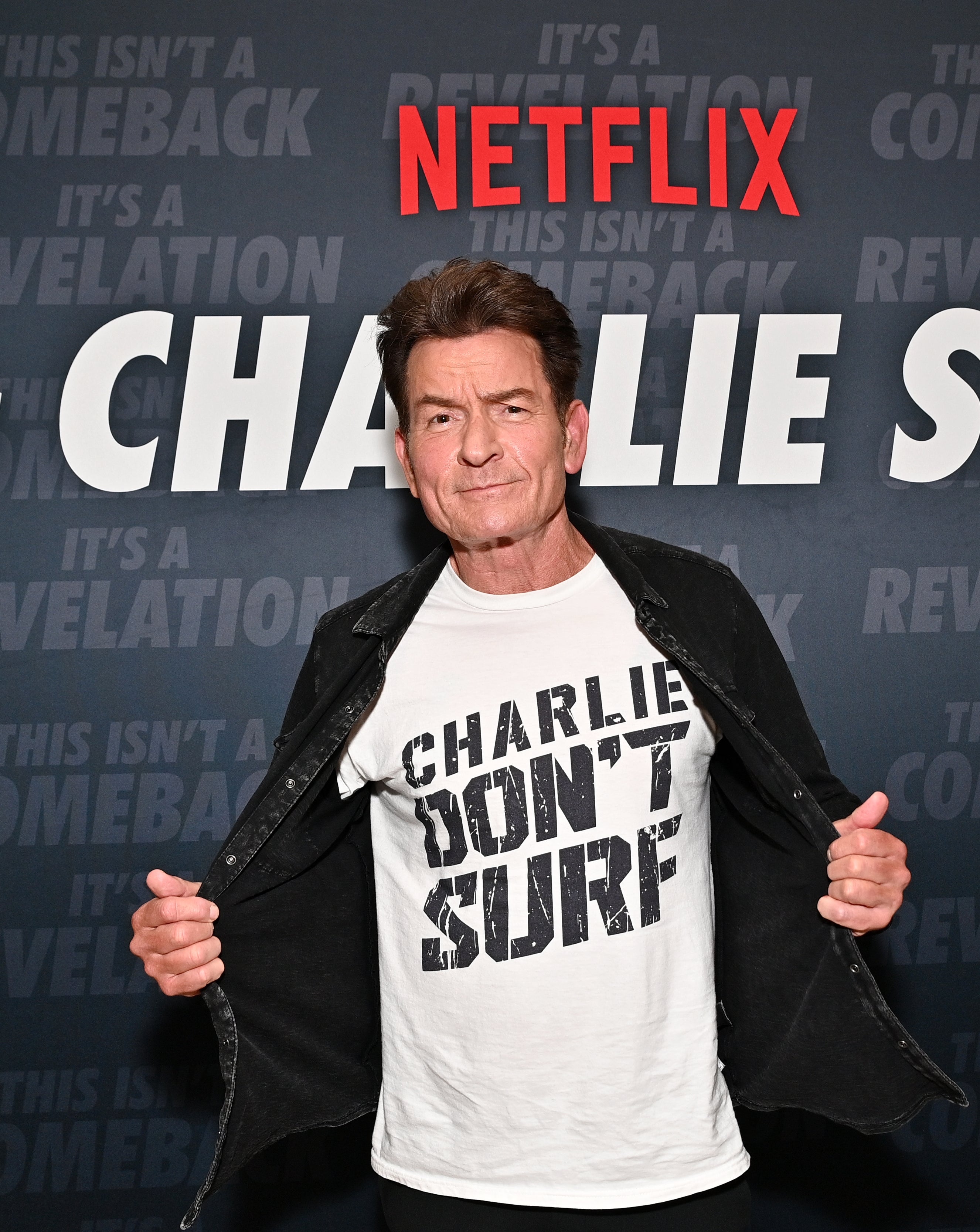 Person wearing a "Charlie Don't Surf" shirt, standing in front of a Netflix-themed backdrop with text about a comeback and revelation