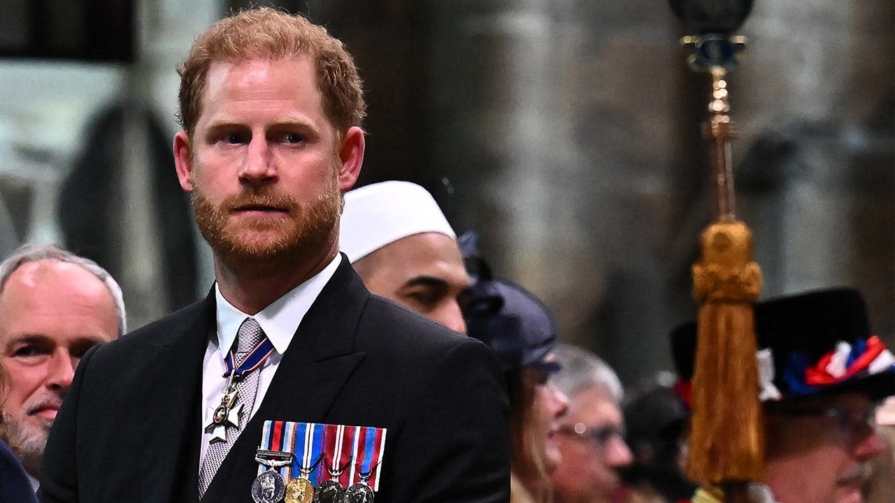 Prince Harry in a dark suit and medals looking up during his father's coronation ceremony.