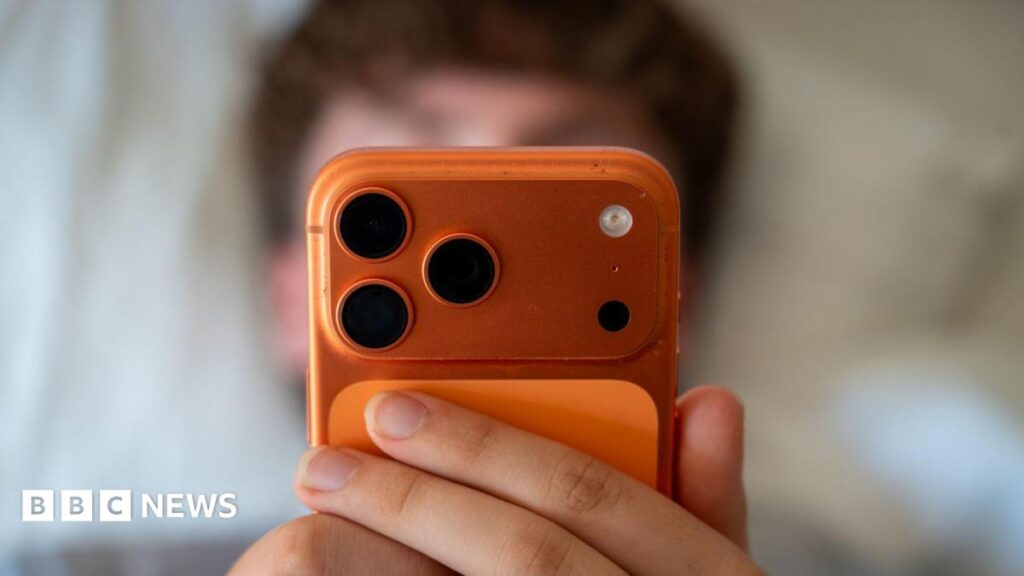 A teenage boy is pictured staring into a phone, suggesting he is using social media.
