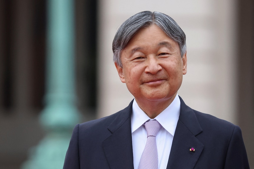 An older Japanese man in a neat suit smiles warmly at the camera.