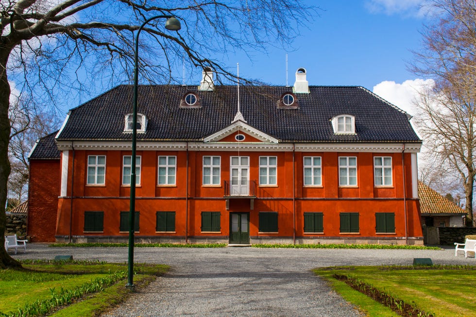 Historic red brick building with dormer windows and a small balcony against a blue sky.
