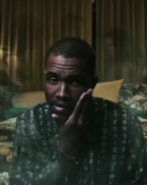 A person in a patterned shirt sits pensively in a dimly lit bedroom with candles in the background