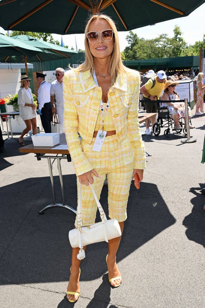 Amanda Holden in a yellow plaid suit, holding a white handbag, stands at an outdoor event.