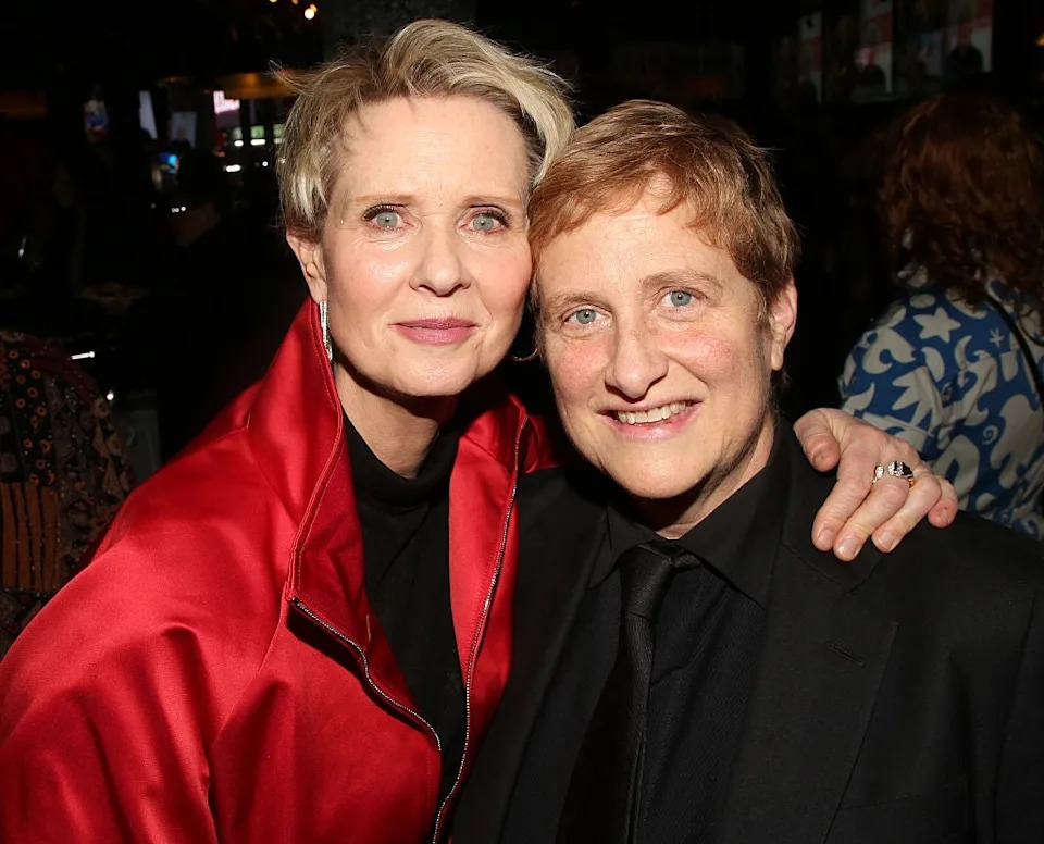 Two individuals smiling at an event; one wears a vibrant jacket, the other a suit. They appear happy and comfortable together