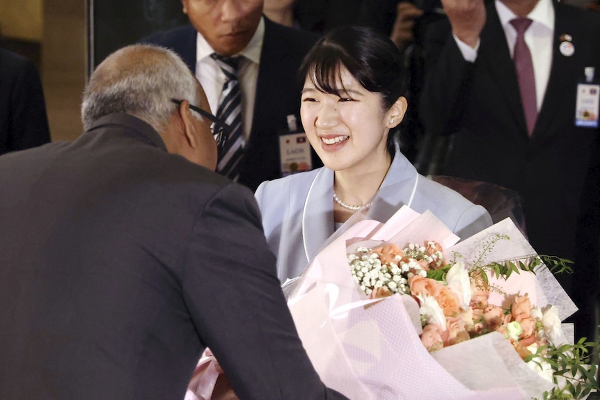 A woman wearing a suit smiles as she is handed a bouquet of flowers