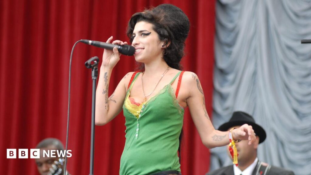 Amy Winehouse’s dad Mitch ordered to pay £1m to singer’s friends A woman with long, blonde hair talks into a microphone