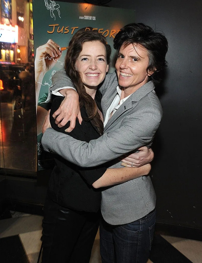 Two individuals happily pose together, both with friendly expressions. One wears a suit jacket, and they appear to be at a public event