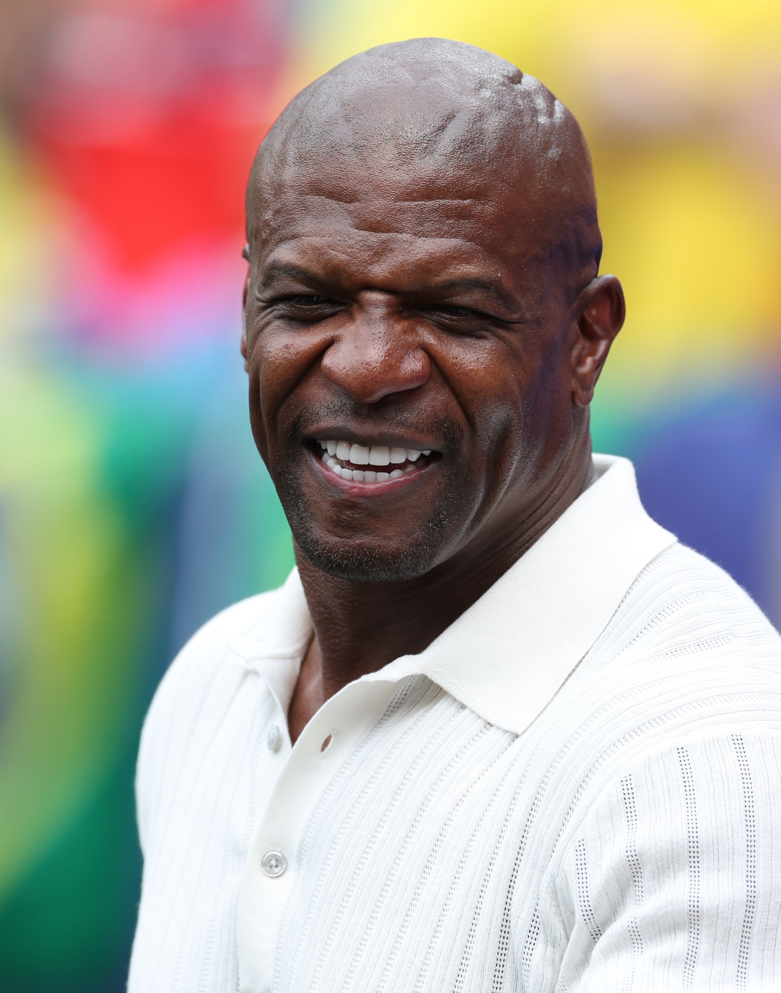 Terry Crews smiling broadly, wearing a white ribbed-knit polo shirt