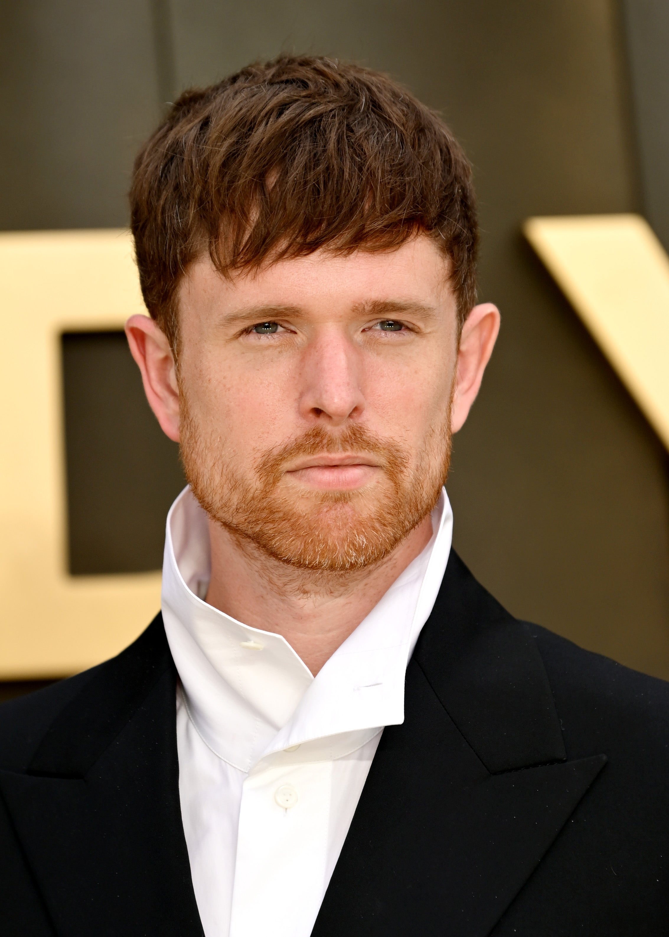 A person on the red carpet wearing a tailored black suit with a unique high-collar white shirt