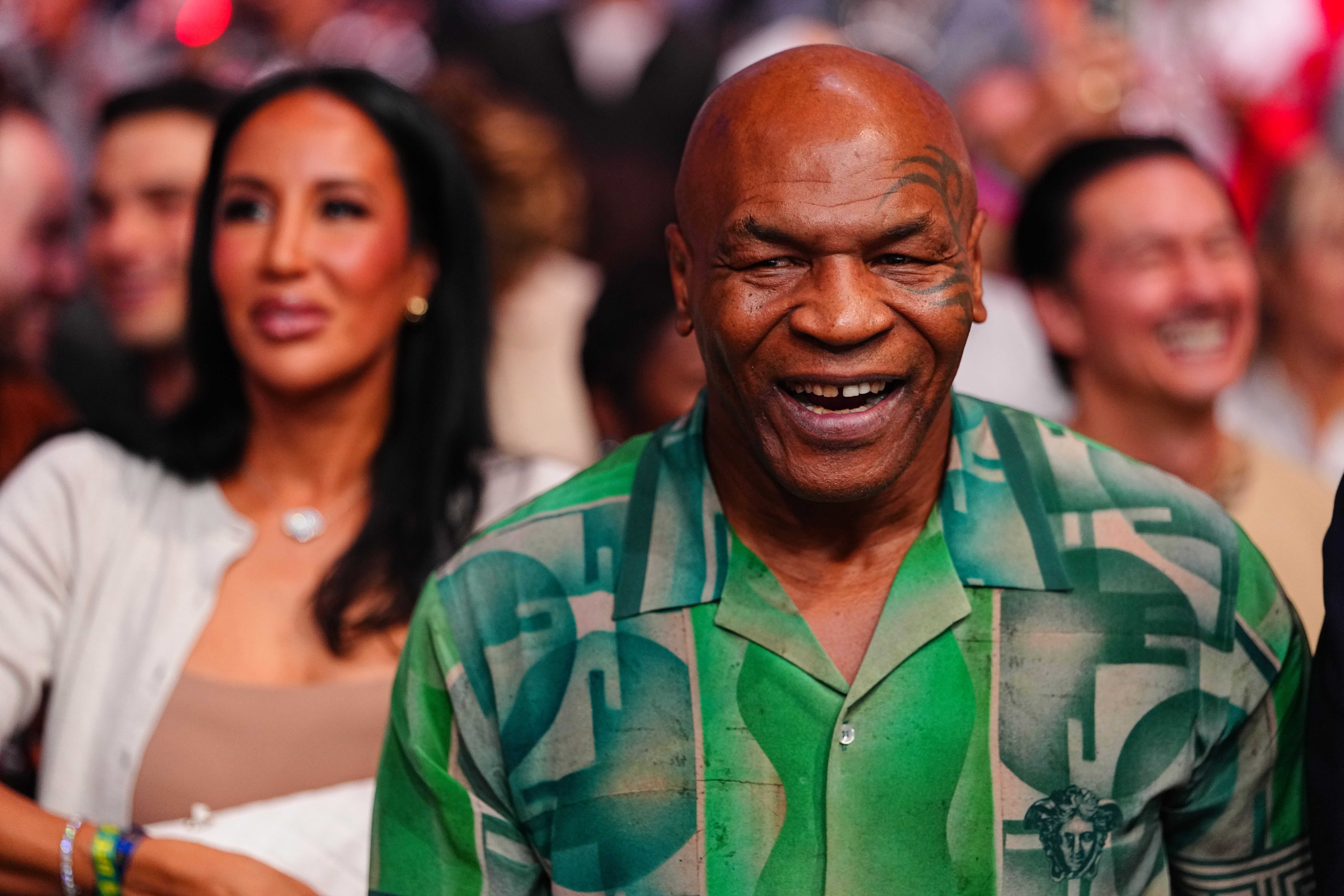 Mike Tyson smiles in a patterned shirt at a UFC fight, surrounded by a crowd