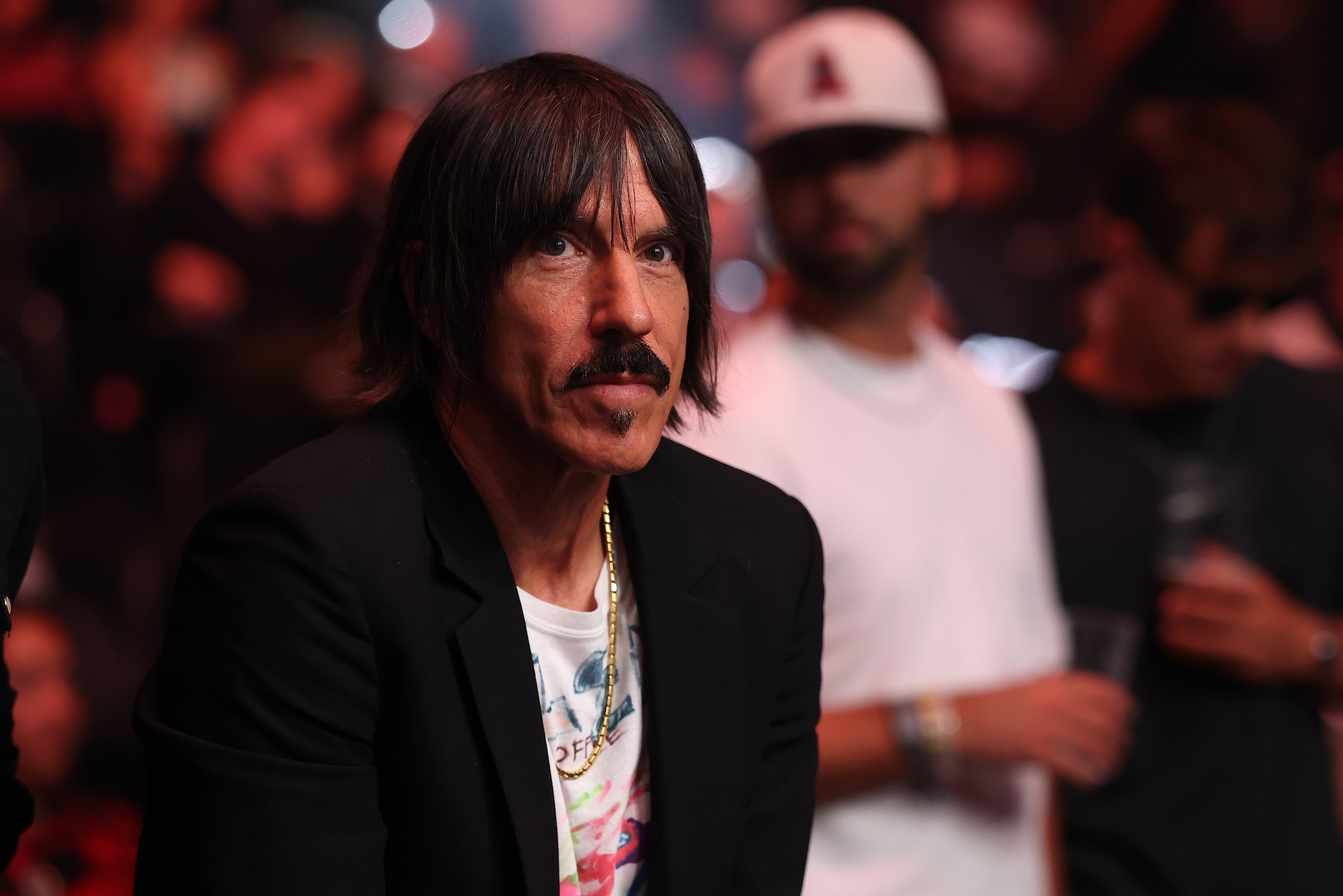 Anthony Kiedis with medium-length hair and mustache in a blazer over a graphic tee at a public event