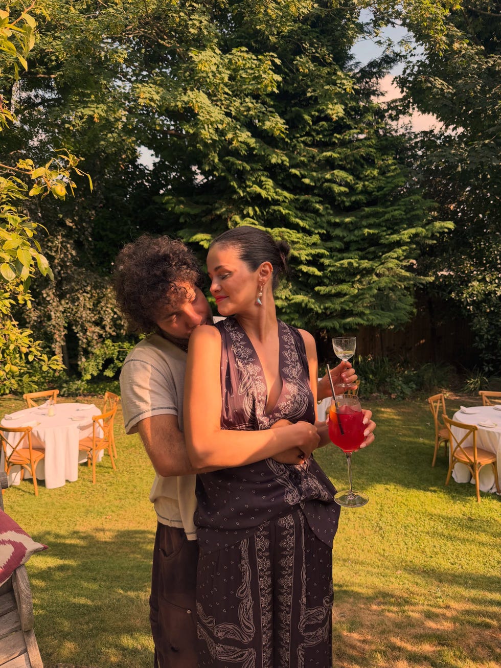 A couple enjoying a summer garden gathering, with one holding a cocktail while embracing the other. A couple enjoying a summer garden gathering, with one holding a cocktail while embracing the other.