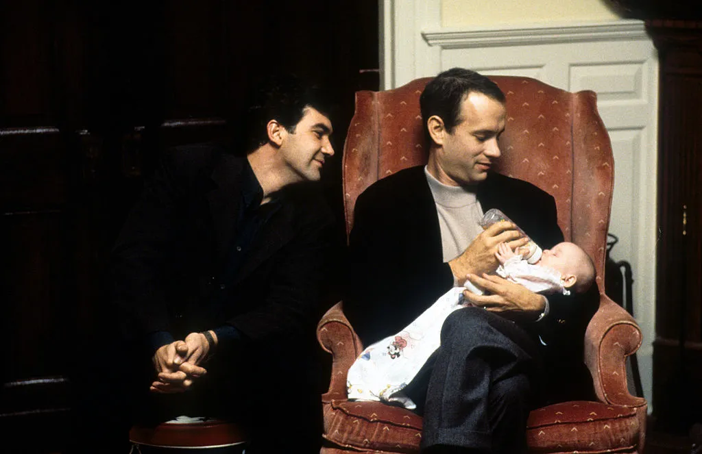 Tom Hanks feeds a baby while Antonio Banderas watches in a scene from the film 'Philadelphia', 1994.