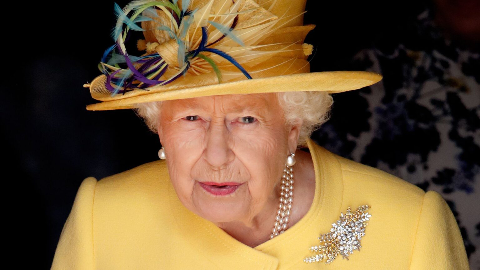 Queen Elizabeth’s Brutal Comeback When Someone Rejected Her Invitation Queen Elizabeth wears a bright yellow coat and a matching hat with purple and blue feathers attached