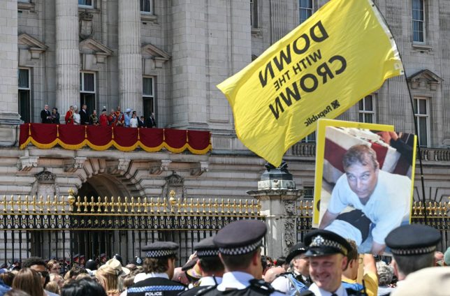 Protestors wave a flag and hold placards as the Royal family watch the flypast on the balcony of Buckingham Palace after attending the King's Birthday Parade "Trooping the Colour" in London on June 13, 2026. (Photo by JUSTIN TALLIS / AFP via Getty Images)