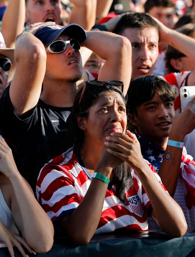 Fans reacting to a soccer game, with a woman in a US soccer jersey holding her hands to her mouth.