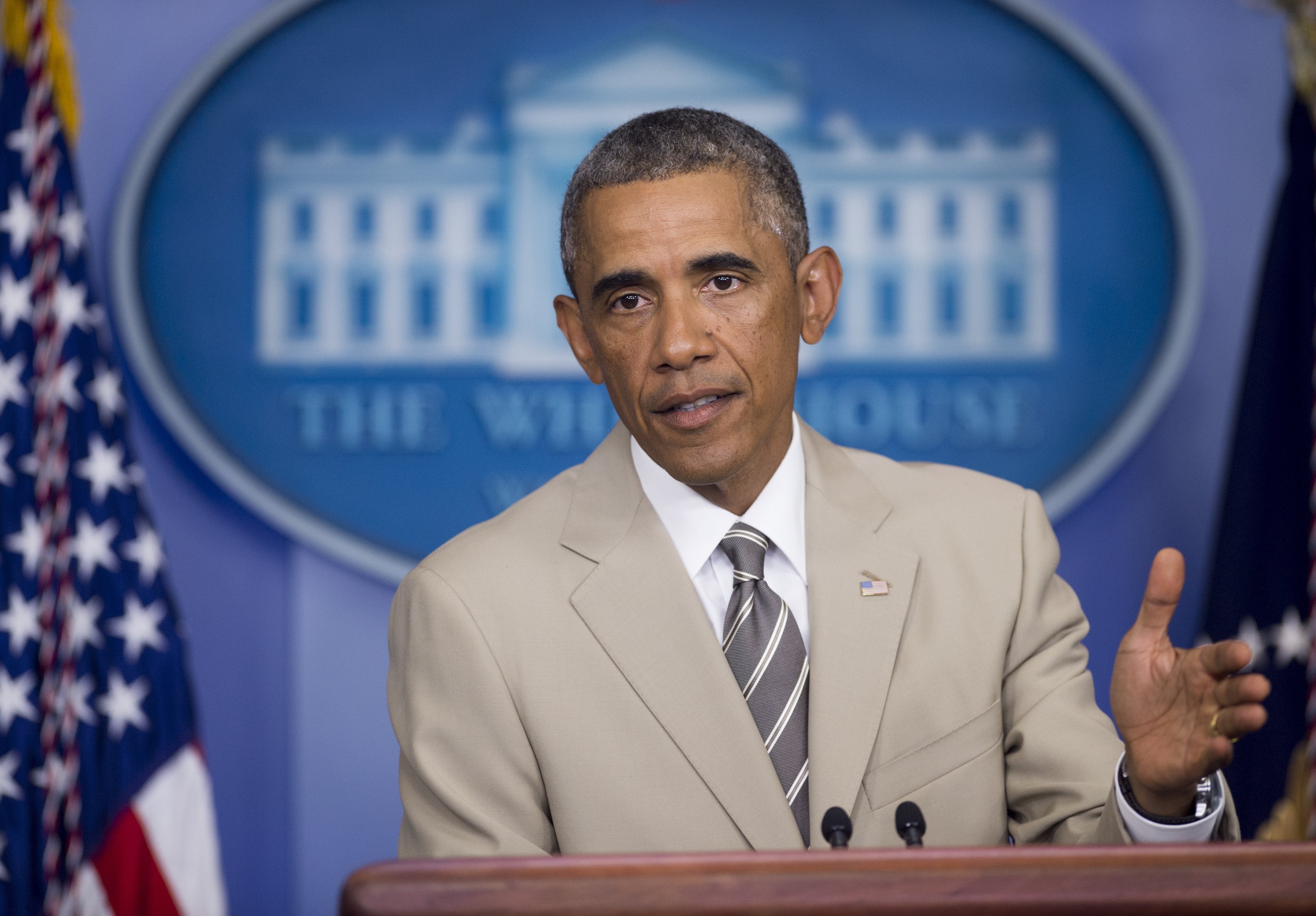 A man in a light suit and striped tie speaks at a podium with a White House emblem in the background