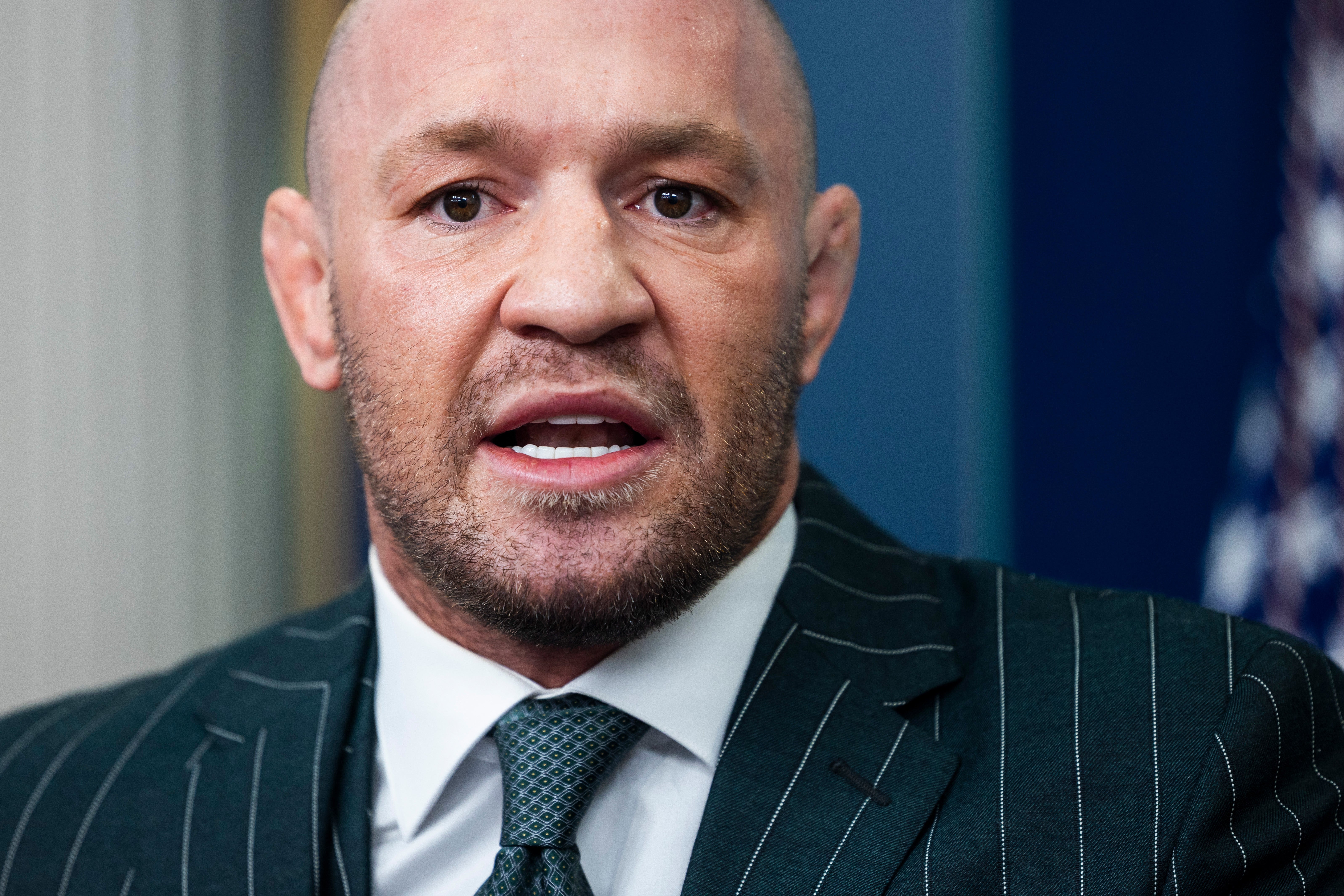Conor McGregor in a pinstripe suit and tie speaks, appearing serious and focused in a professional setting