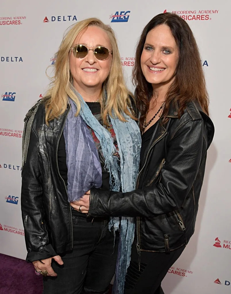 Two people in leather jackets smiling and posing on a red carpet at a MusiCares event