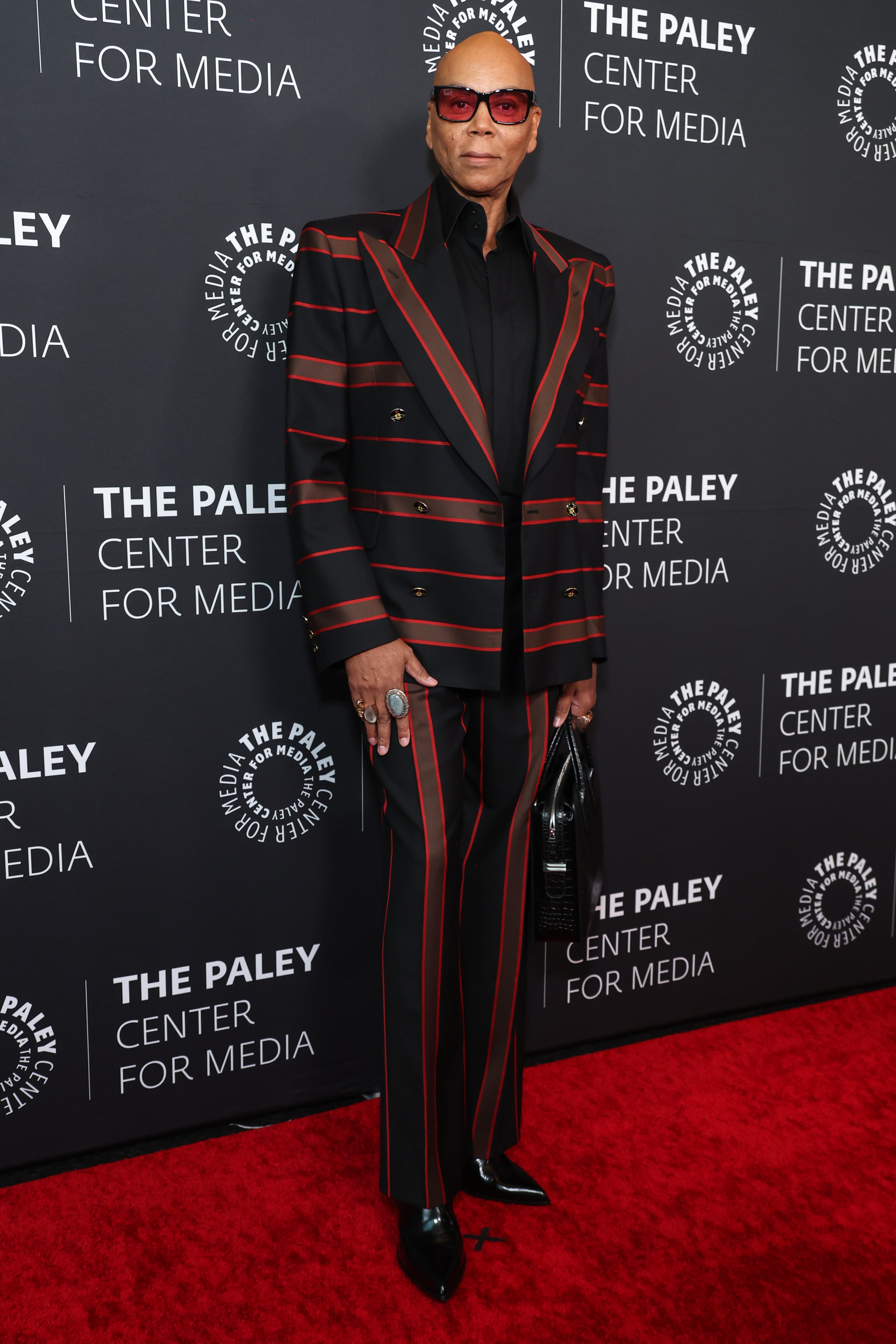 Person wearing a bold pinstriped suit and sunglasses on a red carpet at The Paley Center for Media event
