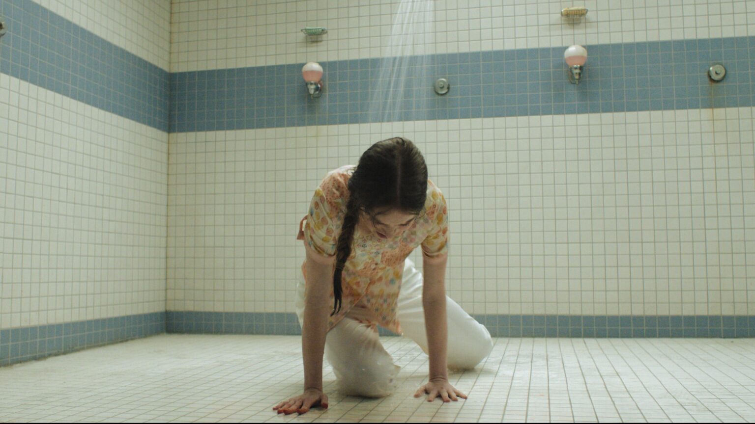 Young girl played by Summer H. Howell crouches on shower floor in high school gym in Carrie TV show.
