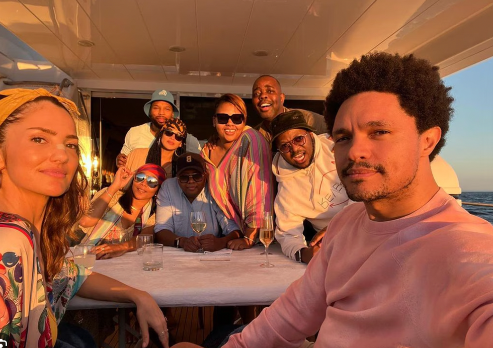 Group of friends enjoying a sunset on a boat, smiling and posing at a table with drinks.