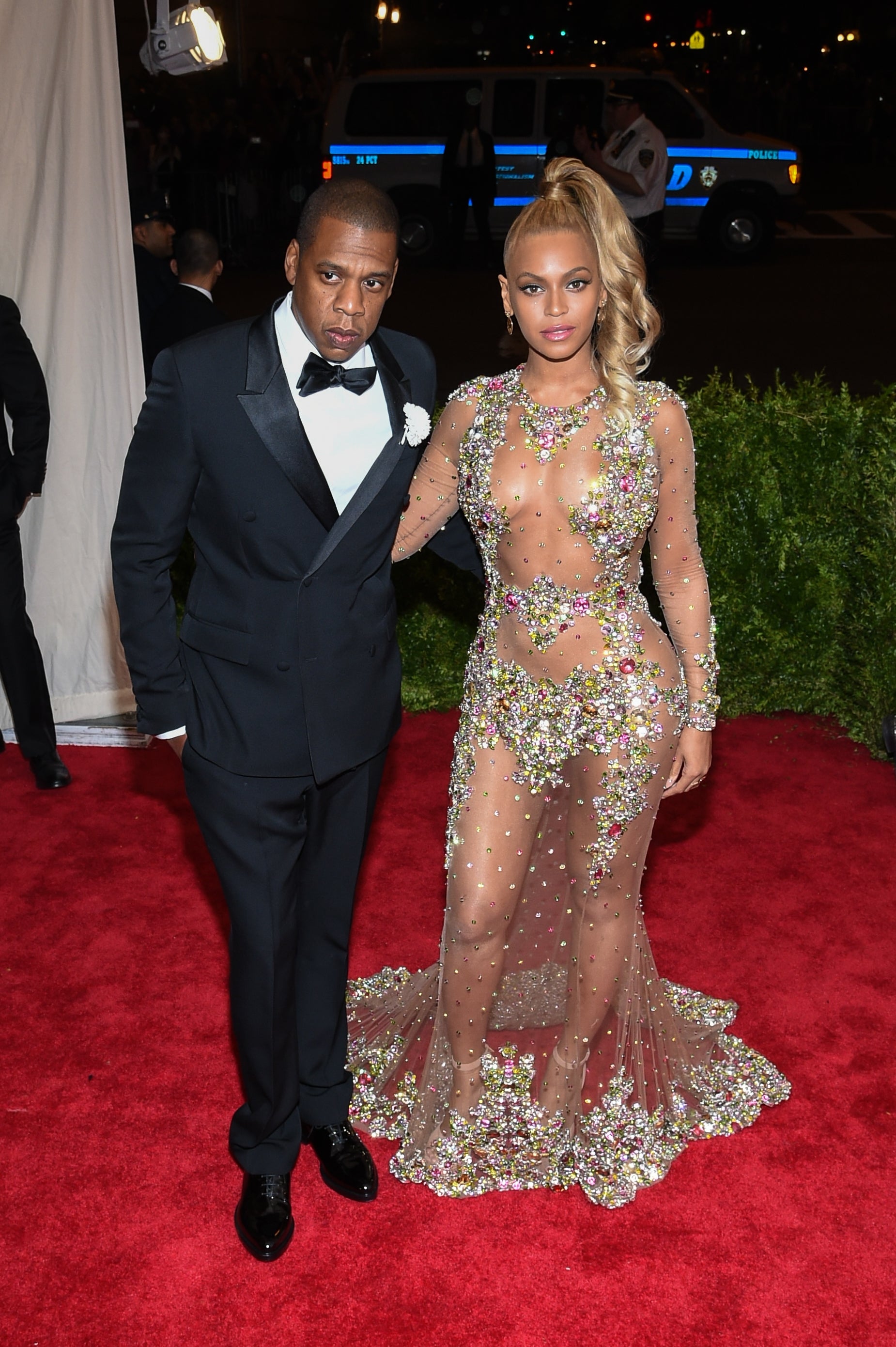 Jay-Z and Beyoncé pose on the red carpet at the 2015 Met Gala. Jay-Z wears a tuxedo, and Beyoncé wears a sheer, jeweled dress