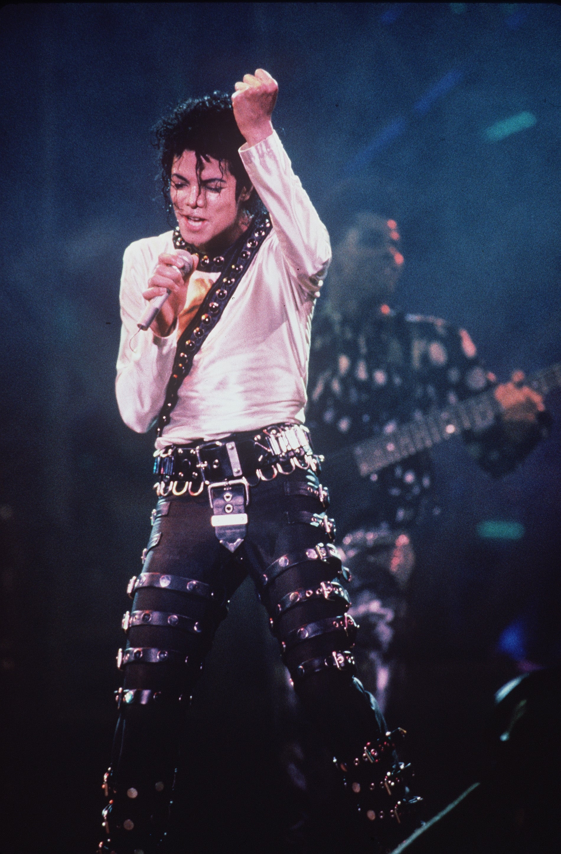 Michael Jackson on stage in iconic leather outfit with numerous buckles and studs, striking a dynamic pose during a live concert