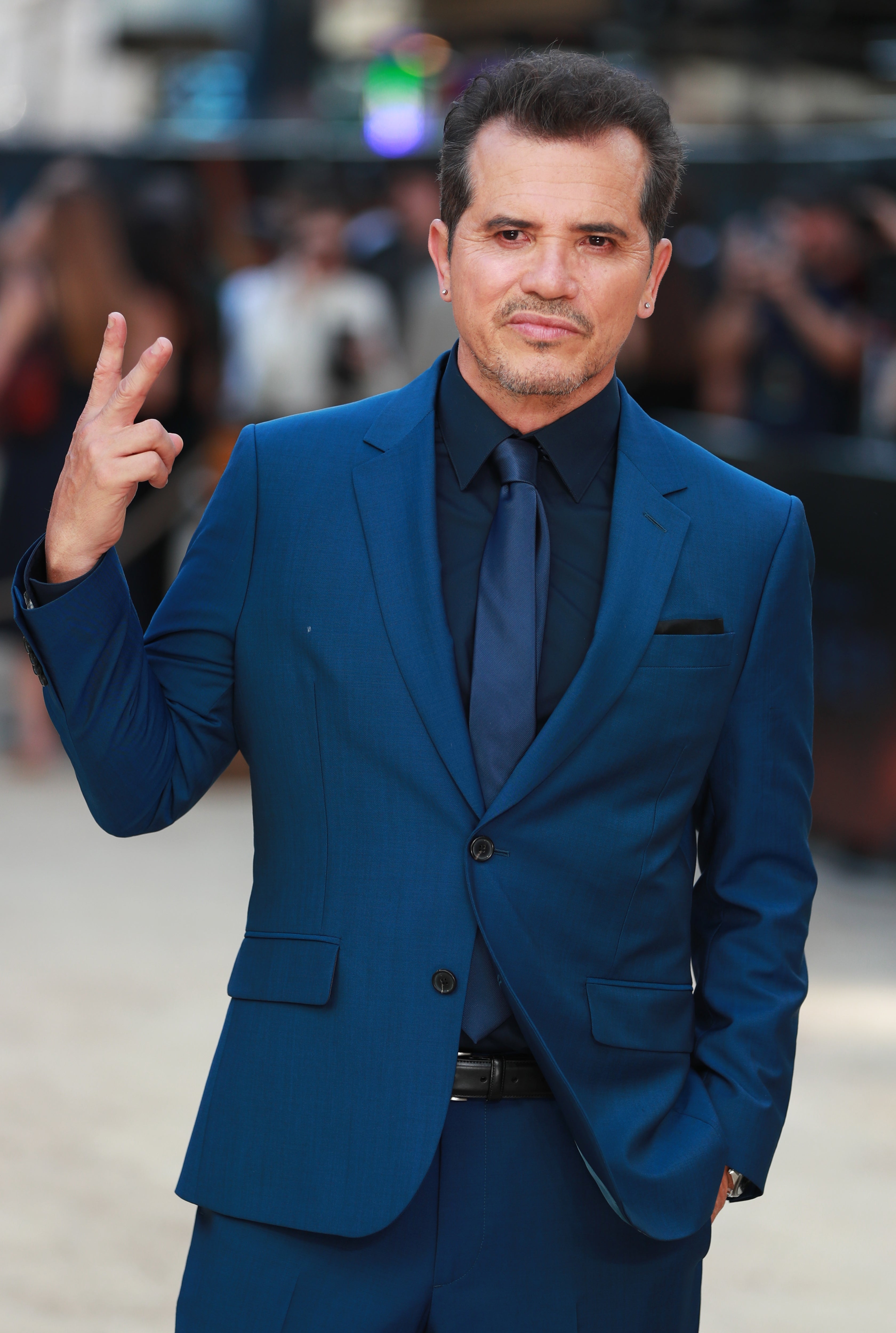 Man in a sharp suit flashes a peace sign on a red carpet at a celebrity event