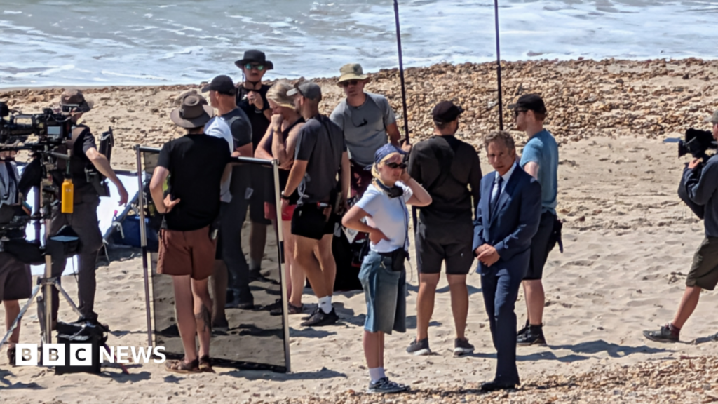 US actor Ben Stiller spotted with film crews on Dorset beach A woman with dark hair pulled back from her face points to a plaster on her arm