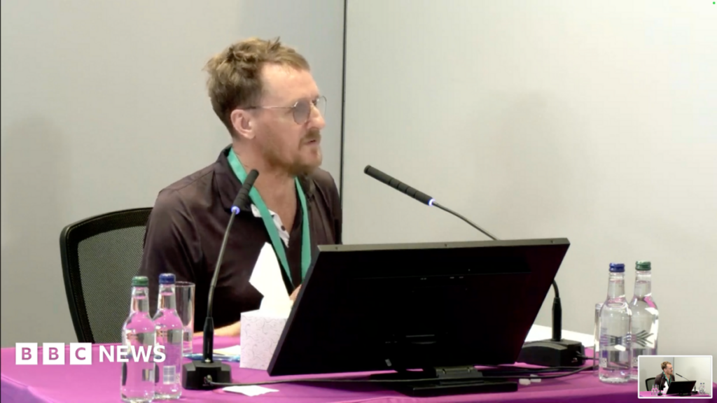 Ex-NHS nurse tells Lampard Inquiry staff apathy ‘astonishing’ Stuart Ayris looks towards Baroness Lampard. He is wearing a black polo shirt and is sitting in front of a purple table with a laptop in front of him. He is wearing a green lanyard and has bottles of water in front of him. He is sitting in the inquiry room, with a microphone in front of him at Arundel House in central London
