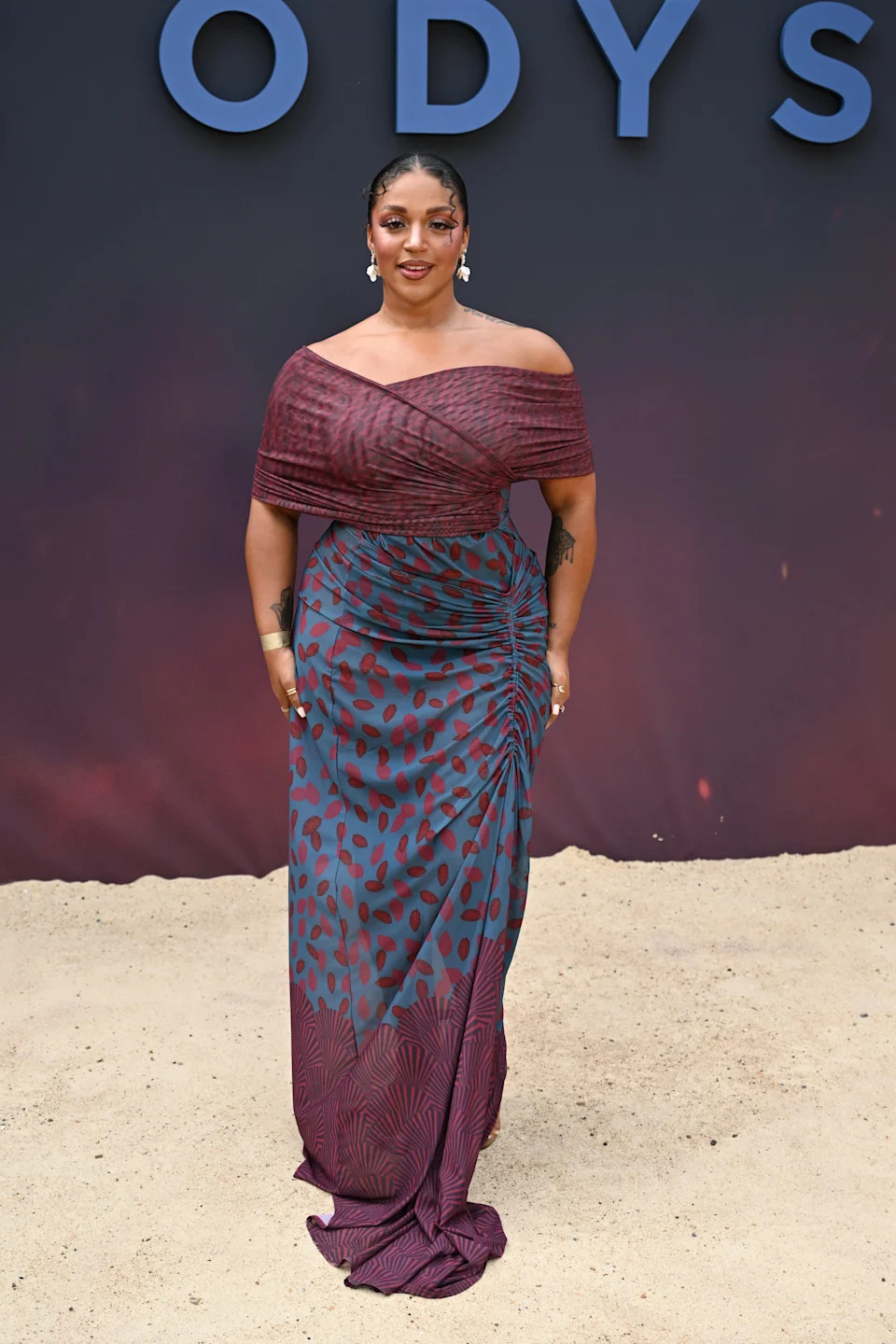 Person in an elegant off-shoulder gown with a patterned skirt at a formal event, posing in front of a backdrop