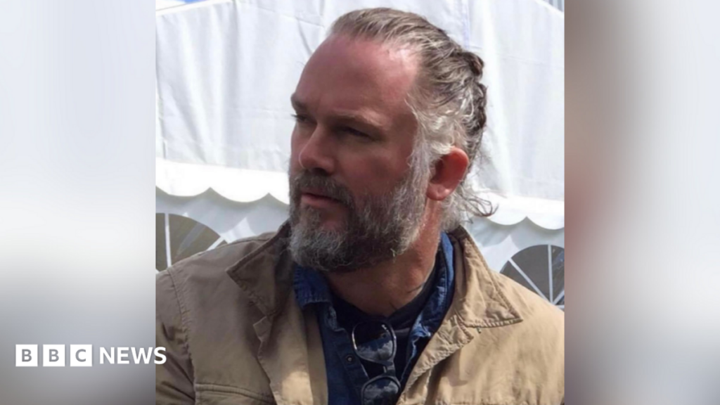 Tributes to Kim Kardashian’s bodyguard killed in motorbike crash A man with a grey beard and hair tied back looking to the side. He is wearing a beige jacket and a blue shirt with sunglasses hanging on.