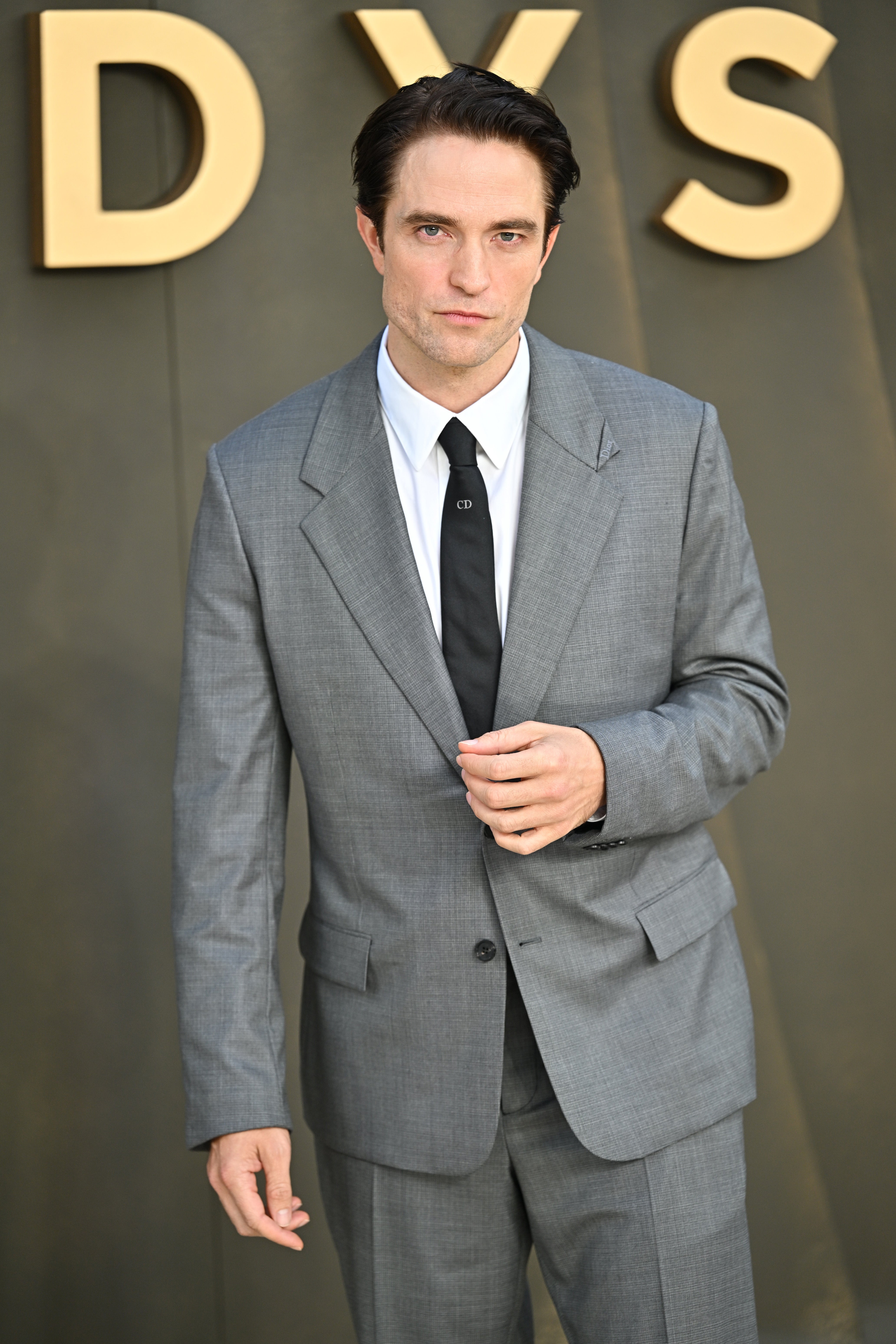 Person in a tailored gray suit with a white shirt and black tie at a formal event