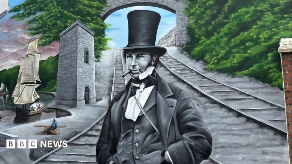 A mural of Isambard Kingdom Brunel on the side of a building. He wears a top hat, waistcoat and coat, with a cigar in his mouth, and stands in front of a railway track and a bridge. Above the bridge are the words 'welcome to Llansawel/Briton Ferry'.