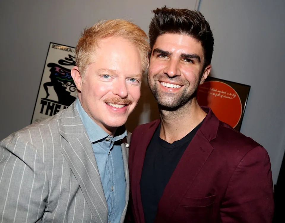 Two people smiling, one in a striped suit and the other in a blazer. They are standing close together, seemingly at an event