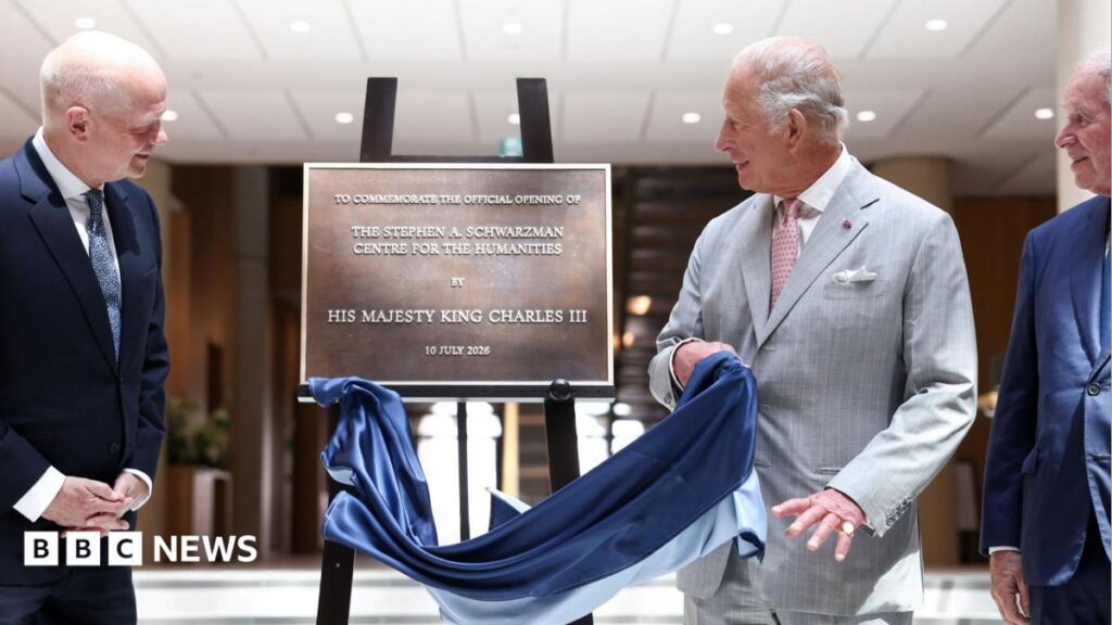 King Charles in a grey suit swiping a cloth off a plaque for the Stephen A Schwarzman Centre for the Humanities.