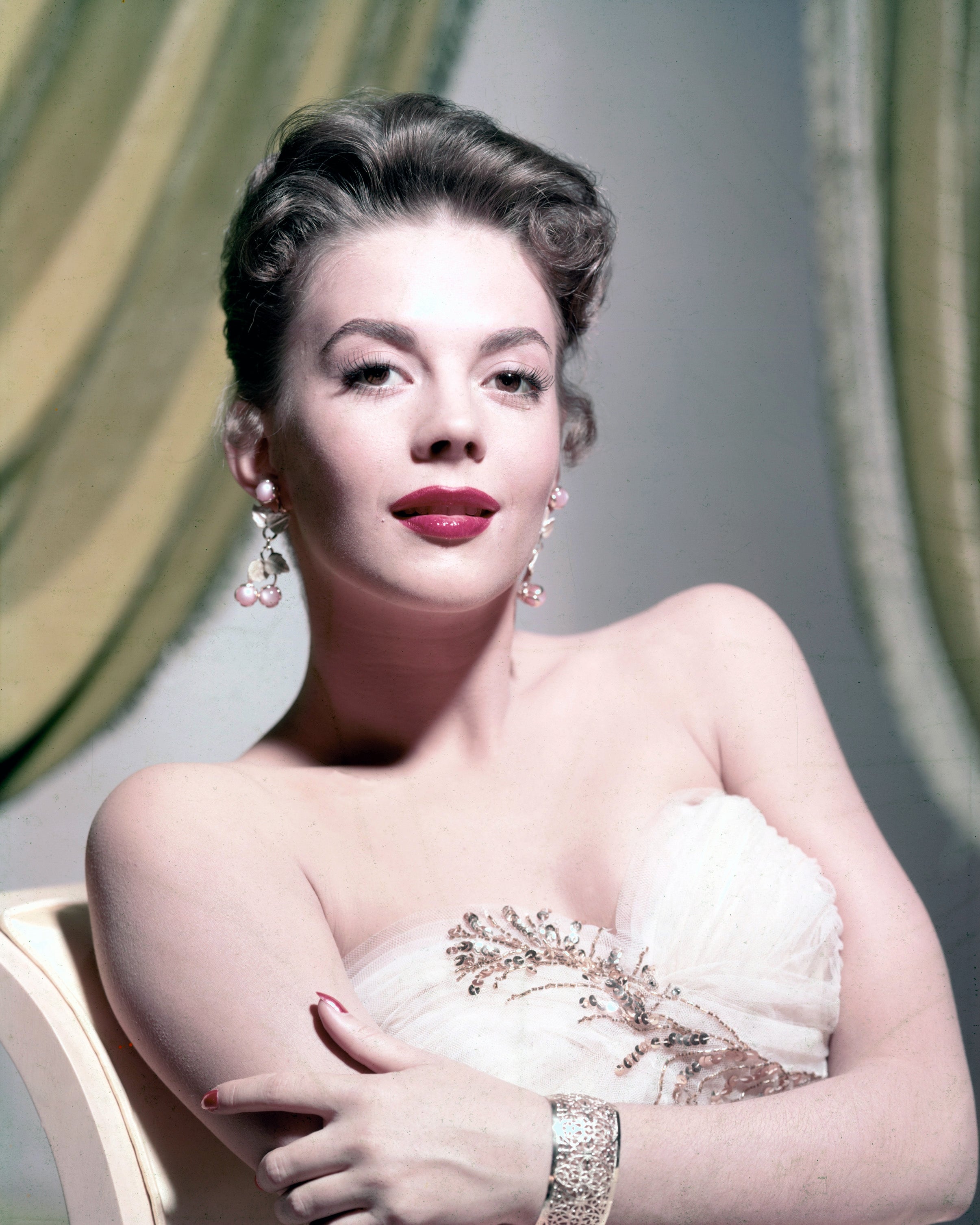 Natalie Wood posing elegantly, wearing a strapless gown with floral details and statement earrings, exuding classic glamour against a draped backdrop