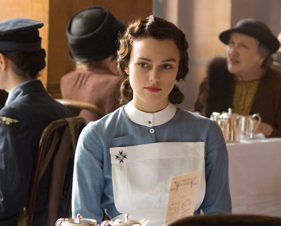keira knightley as cecilia tallis in a blue dress with a white apron seated at a table in a dining setting in movie atonement