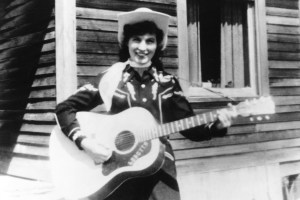 CIRCA 1960: Loretta Lynn holds her acoustic guitar as she poses for a portrait wearing a cowboy hat, a scarf and western shirt outside a log cabin in circa 1960. (Photo by Michael Ochs Archives/Getty Images)