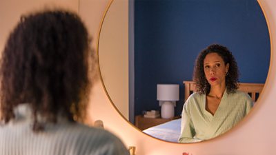 Vinette Robinson as Erica in Time Series 3. She sits in a bedroom at a dressing table and looks in the mirror.