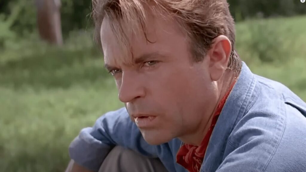 ruggen paleontologist in blue shirt and red kerchief looking intently off to the side while sitting in a jungle clearing