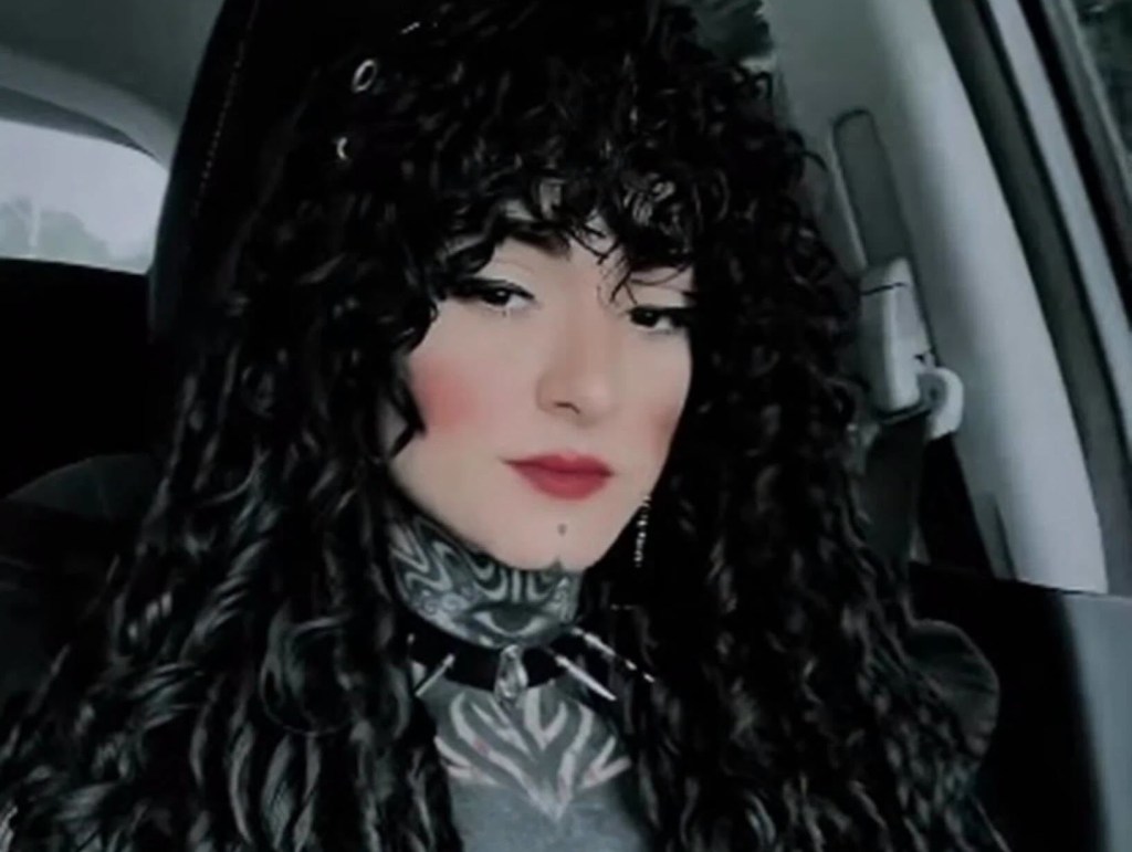 Ulissias Marcelli, a Brazilian influencer, wearing heavy makeup, dark curly hair, tattoos, and a spiked choker.