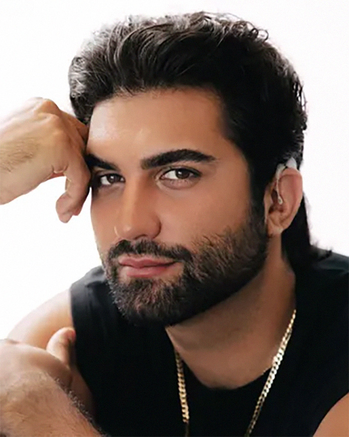 A close-up of a man with dark hair and a beard, wearing a black shirt and a gold chain, for Zendaya's latest look.
