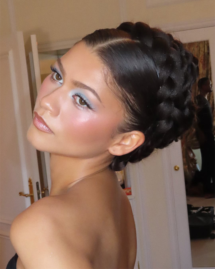 Zendaya's latest look features a intricate braided updo and elegant blue eye makeup, captured in a candid shot.