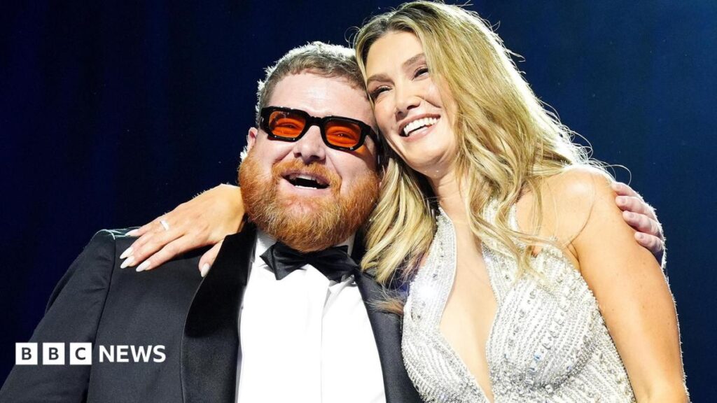 Fife singer Cammy Barnes on his weekend of “absolute madness” A smiling Cammy Barnes, who is wearing a dinner suit, is hugged by Delta Goodrem, who is wearing a silver sparkly dress. Cammmy has ginger hair and beard and black framed glasses with red lenses. Delta has long blonde hair.